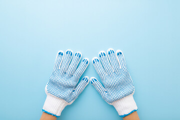 Hands in white textile protective work gloves with anti slip rubber on light blue table background. Pastel color. Closeup. Point of view shot. Top down view.
