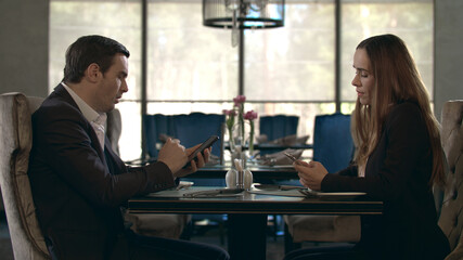 Business couple using mobile phone in restaurant. Couple with smartphones
