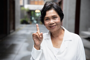 happy smiling Asian senior woman pointing up 1 finger