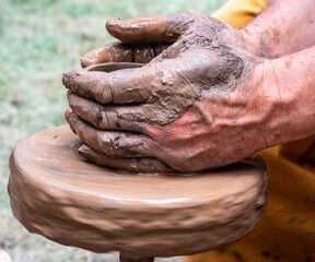 Outdoor pottery workshop. Close-up - the hands of a worker sculpting an earthen vessel on a potter's wheel.