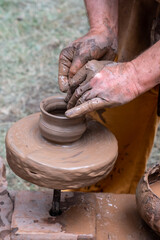 Outdoor pottery workshop. Close-up - the hands of a worker sculpting an earthen vessel on a potter's wheel.