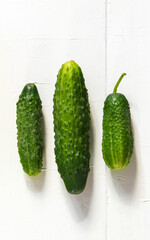 Three fresh green cucumbers of different shapes lie on a white wooden background