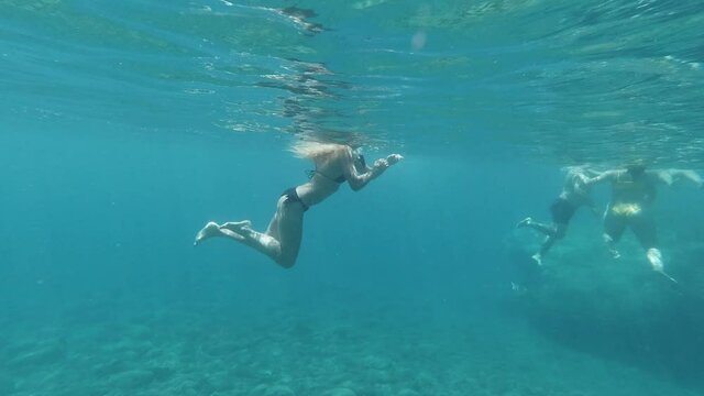 slow motion underwater side view of blond adult group swimming in ocean