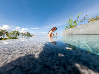 asian woman in bikini in infinity swimming pool edge. luxury vacation near the sea.