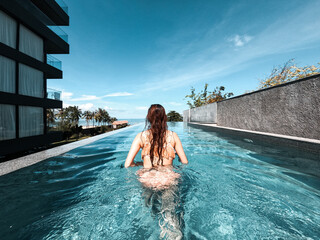 asian woman in bikini in infinity swimming pool edge. luxury vacation near the sea.