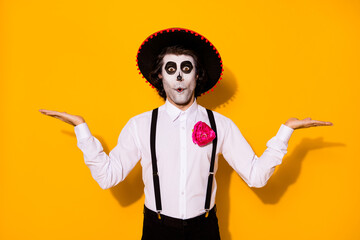 Photo of creepy zombie guy hands hold two hands empty space excited surprise good options dead men wear white shirt death costume sugar skull suspenders isolated yellow color background