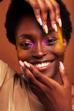 young pretty african girl with bright colorful makeup and manicure posing cheeful on brown background, lifestyle people concept