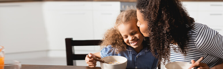 horizontal image of african american woman kissing daughter during breakfast