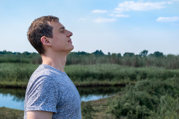 Relaxed adult man breathing fresh air outdoors with lake and field in the background