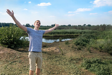 Fototapeta premium Happy man breathing deeply fresh air standing against lake and field a sunny day