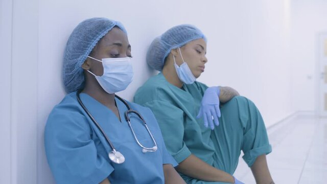 Two overworked female doctors having rest on floor, tired of long surgery, sad