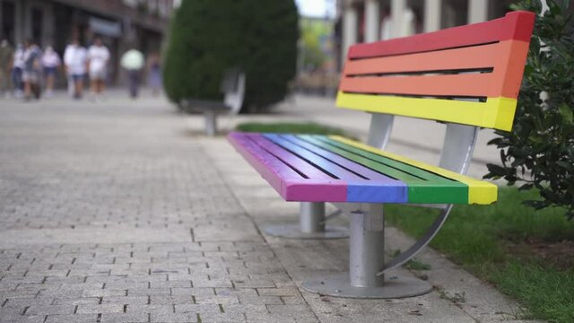 City Bench painted with the colors of Rainbow LGBT gay pride flag. People walking in a Gay Friendly Town