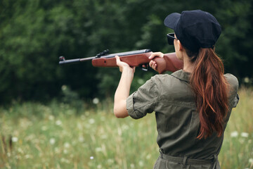 Woman soldier Holds a gun in his hands aiming rear view weapons green trees 