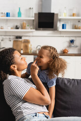 young african american mother touching nose of excited daughter while having fun at home