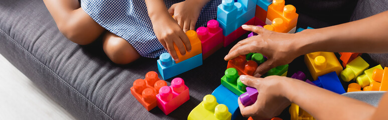cropped view of african american babysitter and girl playing with multicolored building blocks,...
