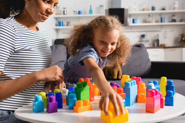 selective focus of african american girl taking building block while playing together with young nanny