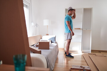 Man assembling furniture in new apartment, moving in and being hardworking.