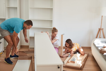 Mother, father, and daughter assembling furniture in new apartment, moving in and being hardworking.