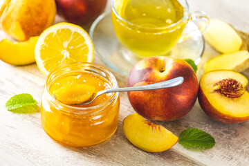 Fresh homemade peach jam in glass jar on a light gray wooden background. Several fresh berries,...