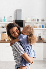 Obraz premium young african american woman with closed eyes holding daughter on hands in kitchen