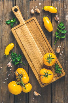 Different raw ripe fresh yellow tomatoes on wooden cutting board. Concept of green house life style and products of subsistence farming, flat lay on dark wooden rustic surface, copy space
