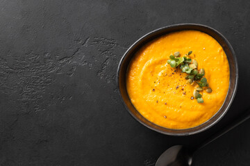 Fall pumpkin soup garnish microgreens in bowl on black background. View from above. Minimal style....