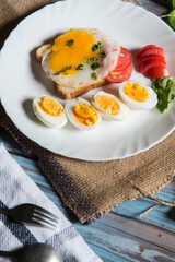 Close up of breakfast ingredients fried egg with bacon and pieces of boiled eggs in a white plate