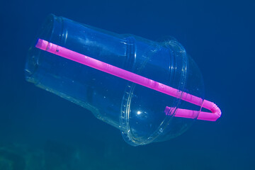 Plastic cocktail cup with a plastic straw slowly drifts underwater in blue water. Budva, Montenegro