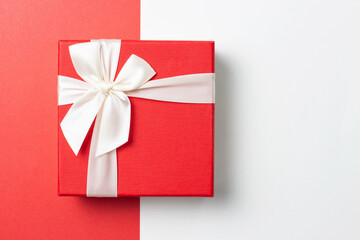 Gift in red box with white ribbon on red and white background, top view
