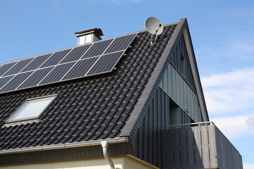 Photovoltaikanlage auf einem Haus mit Balkon, Kaminabdeckung und Satellitenschüssel, bei blauem...