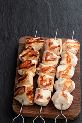Grilled chicken breast fillet on a skewers on black stone background