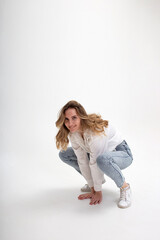 portrait of young smiling caucasian woman posing in shirt and blue jeans, sitting on white studio floor. model tests of pretty girl in casual clothes on cyclorama. attractive female fooling around