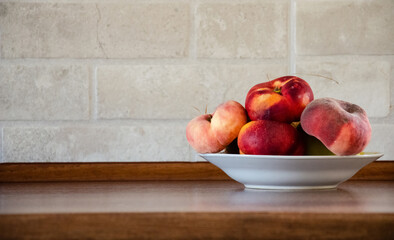 A plate with Saturn peaches on a wooden table in the kitchen. Peaches on a kitchen table against a...