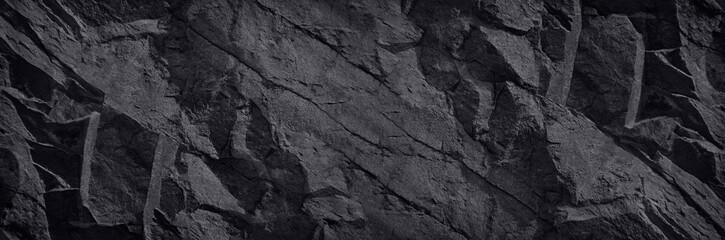 Black stone background. Dark rock texture. Mountain surface texture. Close-up. A wide banner with a volumetric stone texture. Black background with copy space for your design.