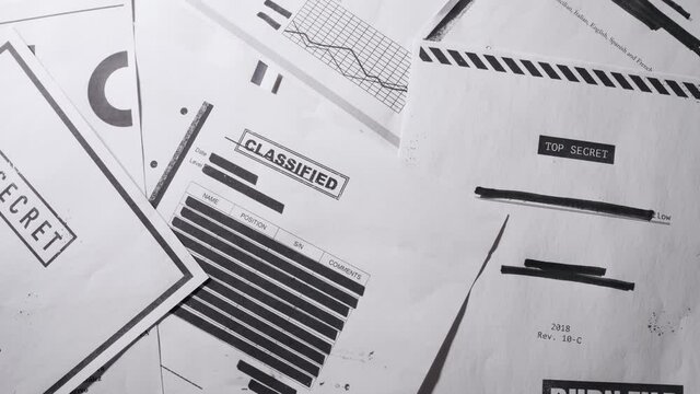 Slow pan top down shot on top secret classified documents laid on table. Important material censored and redacted leaked by whistleblower or informant. Espionage activity or government reports.