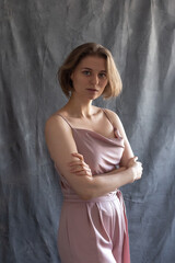 portrait of young caucasian woman with short hair posing in pink suit, standing in front of fabric background. pretty girl in blouse. attractive pensive female poses with arms crossed