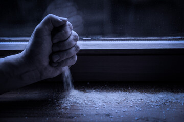 Hand strewing salt on the windowsill, ritual and protection for the evil into the night