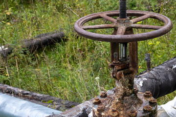 Old rusty valve close up on greenery background.