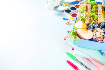 Healthy children school lunch box: sandwich, vegetables ,fruit and mineral water bottle, with school supplies on, on light blue background copy space