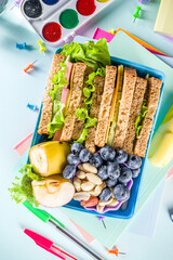 Healthy children school lunch box: sandwich, vegetables ,fruit and mineral water bottle, with school supplies on, on light blue background copy space