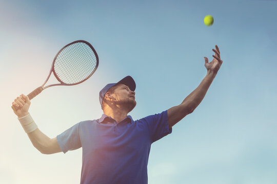 Active Young Man Playing Tennis Outdoors. Serve The Ball Against Blue Sky