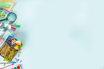 Healthy children school lunch box: sandwich, vegetables ,fruit and mineral water bottle, with school supplies on, on light blue background copy space