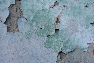 green cracked texture of plaster, with elements of rubbed gray paint. The pastel tone of a textured street wall. Crack in the wall, multiple holes in the old green plaster