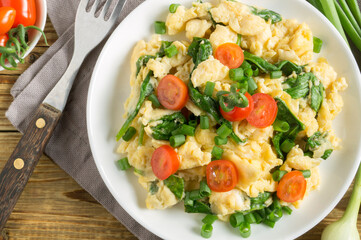 scrambled eggs with spinach and tomatoes on a white plate.