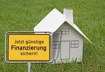 Ortsschild, Kartonhaus „Jezt günstige Finanzierung sichern!“