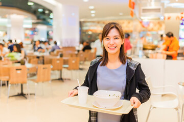 Asian businesswoman eat food at food court and blurry food court at supermarket/mall for background...