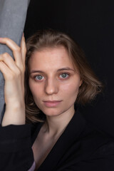 Obraz premium portrait of young caucasian woman with short hair posing in black suit jacket, holding curtain. closeup shot of pretty girl. short-haired attractive female poses in studio