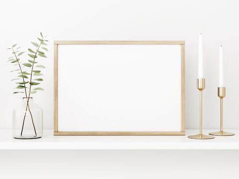 Horizontal poster mockup with wooden frame, eucalyptus branches in vase and brass candle holders on empty white wall background. Minimalist Christmas interior decoration. 3d rendering, illustration.
