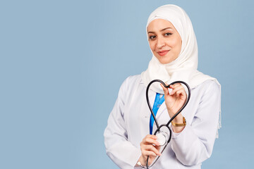 friendly, Muslim doctor or nurse woman in hijab with a heart shaped stethoscope. on a blue background.