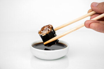 take an unagi maki rolls with bamboo chopsticks and put it into soy sauce on white background, asian food, japanese cuisine